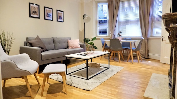Un salon moderne avec un canapé gris, deux fauteuils, une table basse et un coin repas comprenant une table et des chaises.