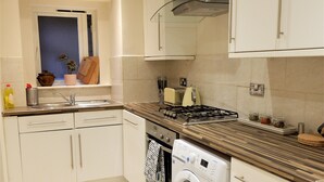 Une cuisine compacte avec des meubles blancs, une cuisinière encastrée, un lave-linge et une fenêtre donnant sur un beau paysage.
