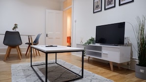 Un salon moderne avec un meuble TV blanc, un téléviseur à écran plat, un canapé blanc et une petite table dotée d’un cadre en métal noir.