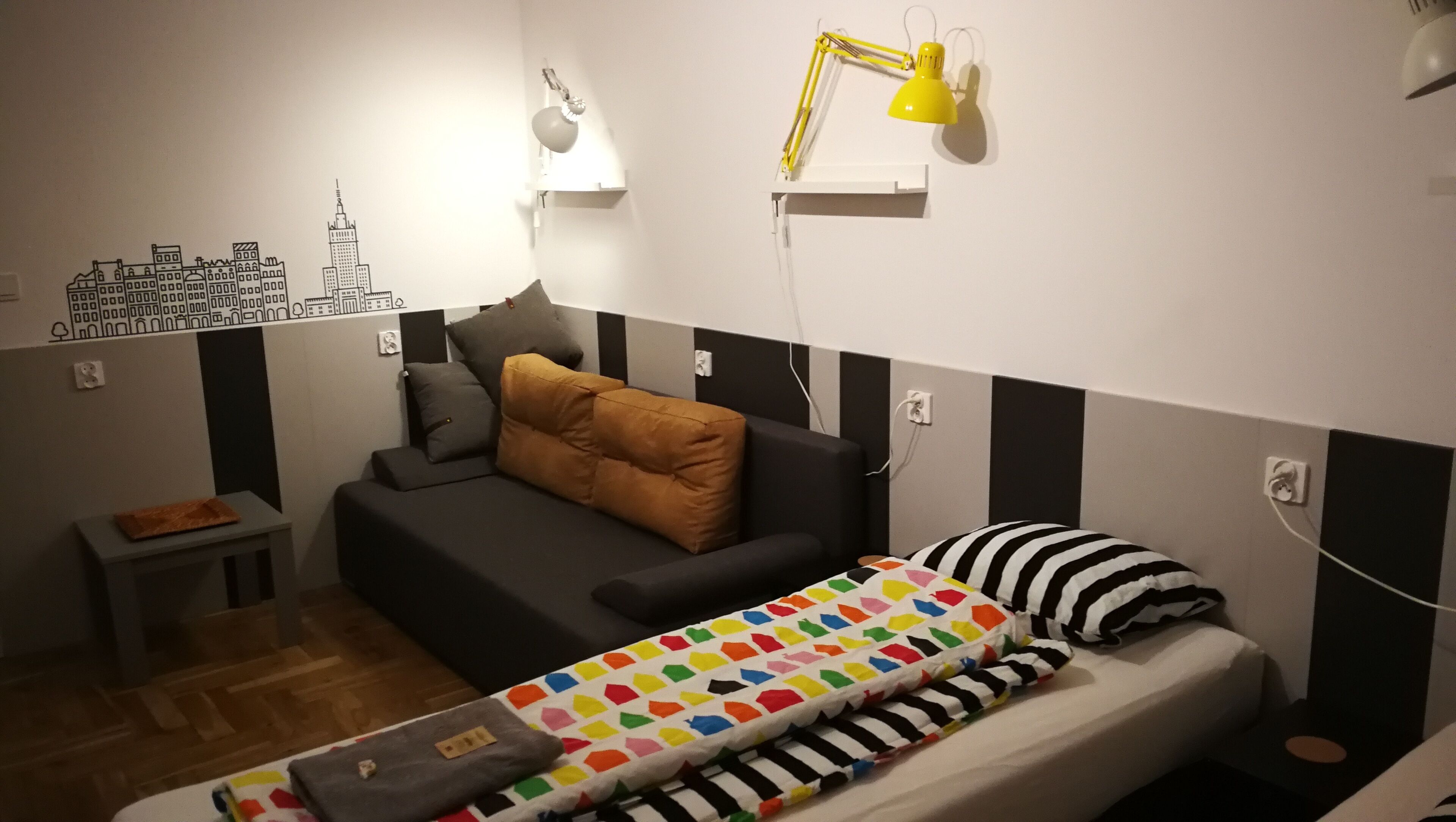 A small, compact room with a bed, a sofa, a desk, and a lamp.