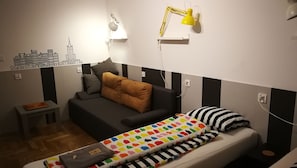 A small, compact room with a bed, a sofa, a desk, and a lamp.