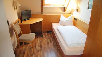 Ein kleines Zimmer mit einem Holztisch, einem Stuhl, einem Bett und einem Fernseher.