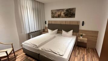 A double bed with white linens, a wooden headboard, a nightstand with a lamp, and a painting above the bed.