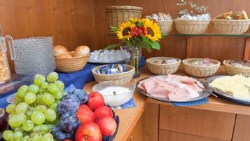 A buffet table with various food items including fruits, bread, and pastries.