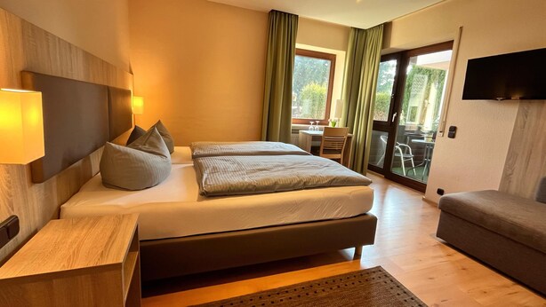 A modern hotel room with a large bed, a sofa, a desk, and a TV. - Annas Gästehaus (Hallerndorf)