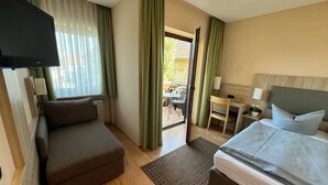 A hotel room with a sofa, a bed, a TV, a desk with a lamp, and a view of the outdoors. - Annas Gästehaus (Hallerndorf)