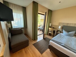 Quarto de hotel com sofá, cama, televisão, escrivaninha com luminária e vista para o exterior.