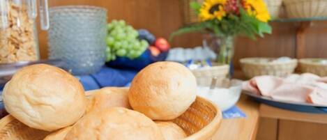 A kitchen counter with a basket of bread rolls, a bowl of grapes, and a vase of sunflowers.