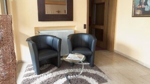 A room with two black leather chairs, a small round table with a magazine, a radiator, and a door leading to another room. - Annas Gästehaus (Hallerndorf)