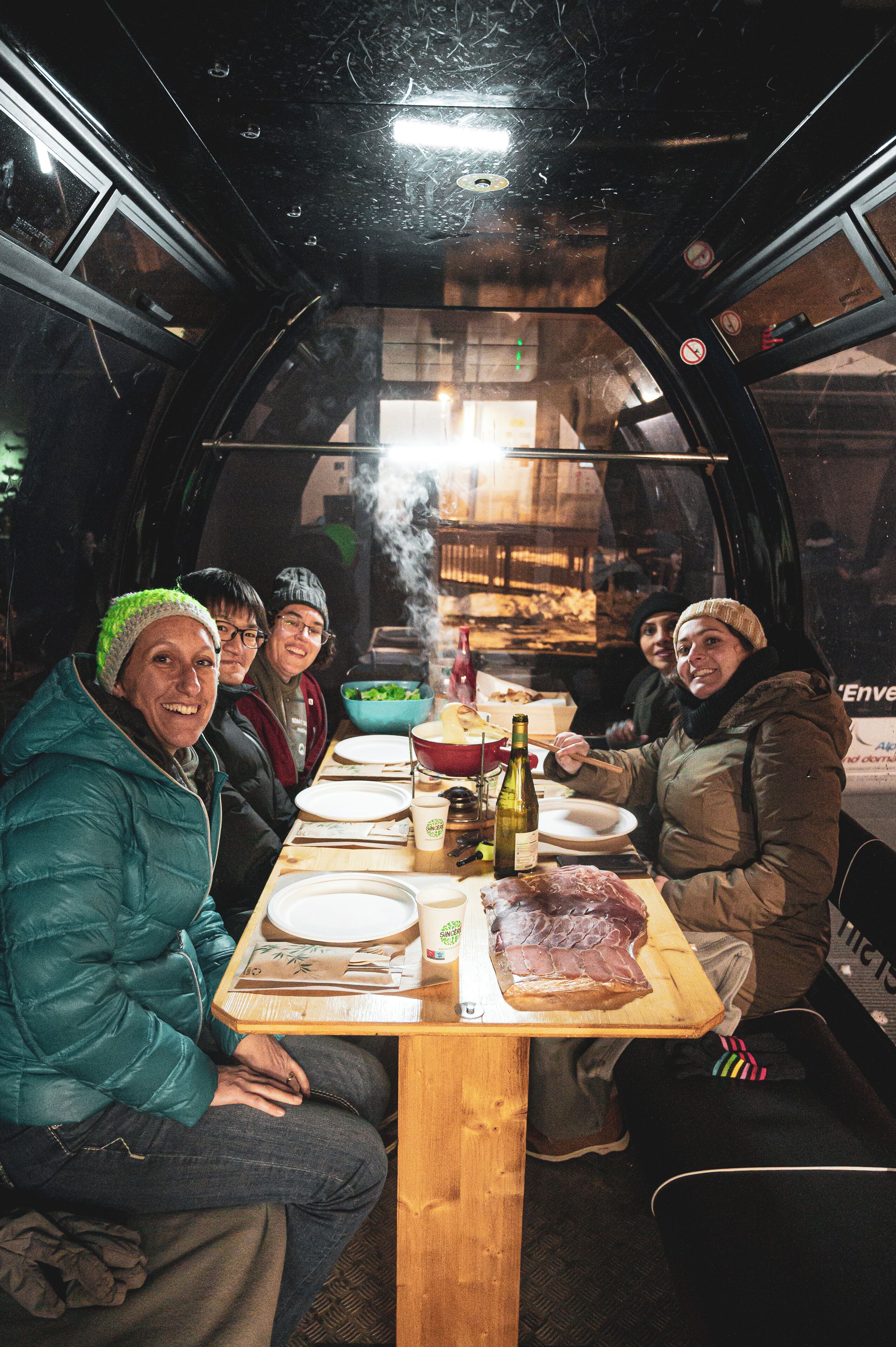 Un grupo de personas sentadas alrededor de una mesa de madera dentro de un vehículo con techo transparente, disfrutando de una comida con diversos platos y bebidas.