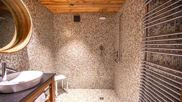 A bathroom with a mosaic tile shower, a wooden vanity with a round mirror, and a tiled floor.