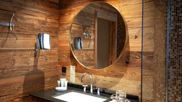 Een badkamer met een houten wand, een ronde spiegel, een wastafel en een glas water op het aanrecht.