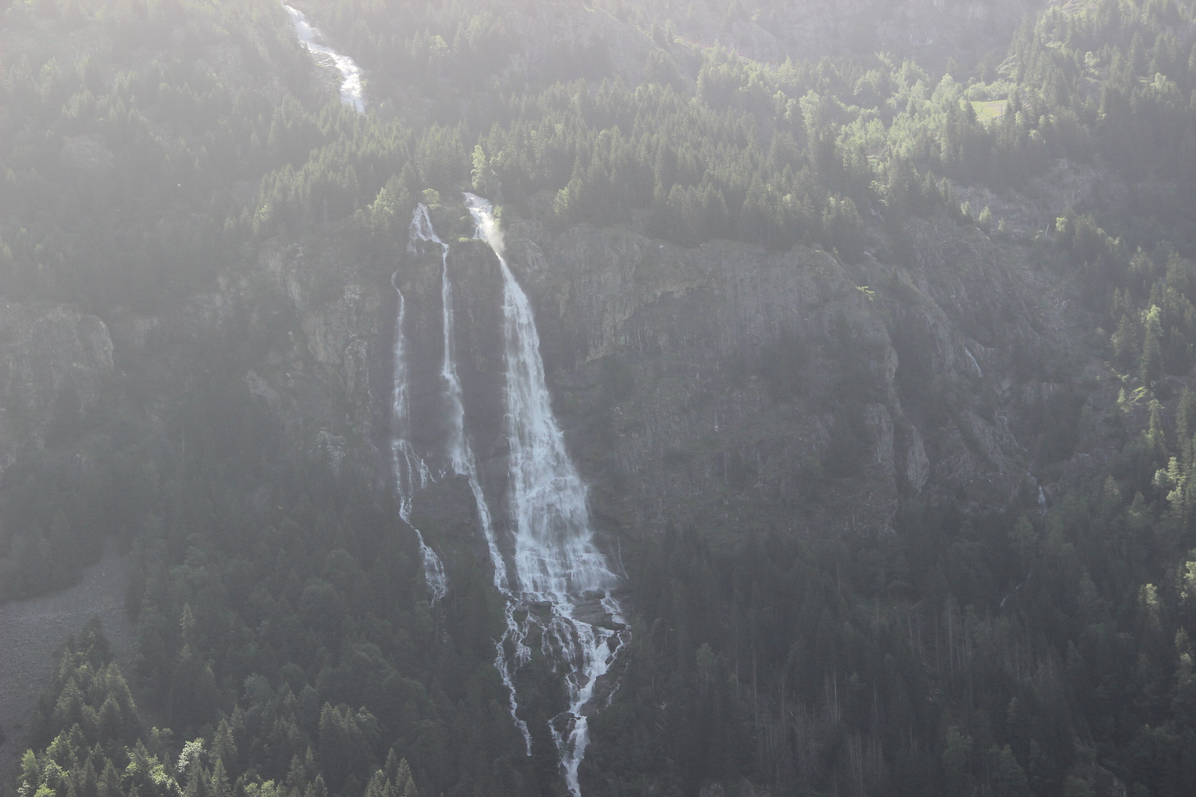 Ein Wasserfall stürzt über eine steile, felsige Klippe, umgeben von dichtem Wald.