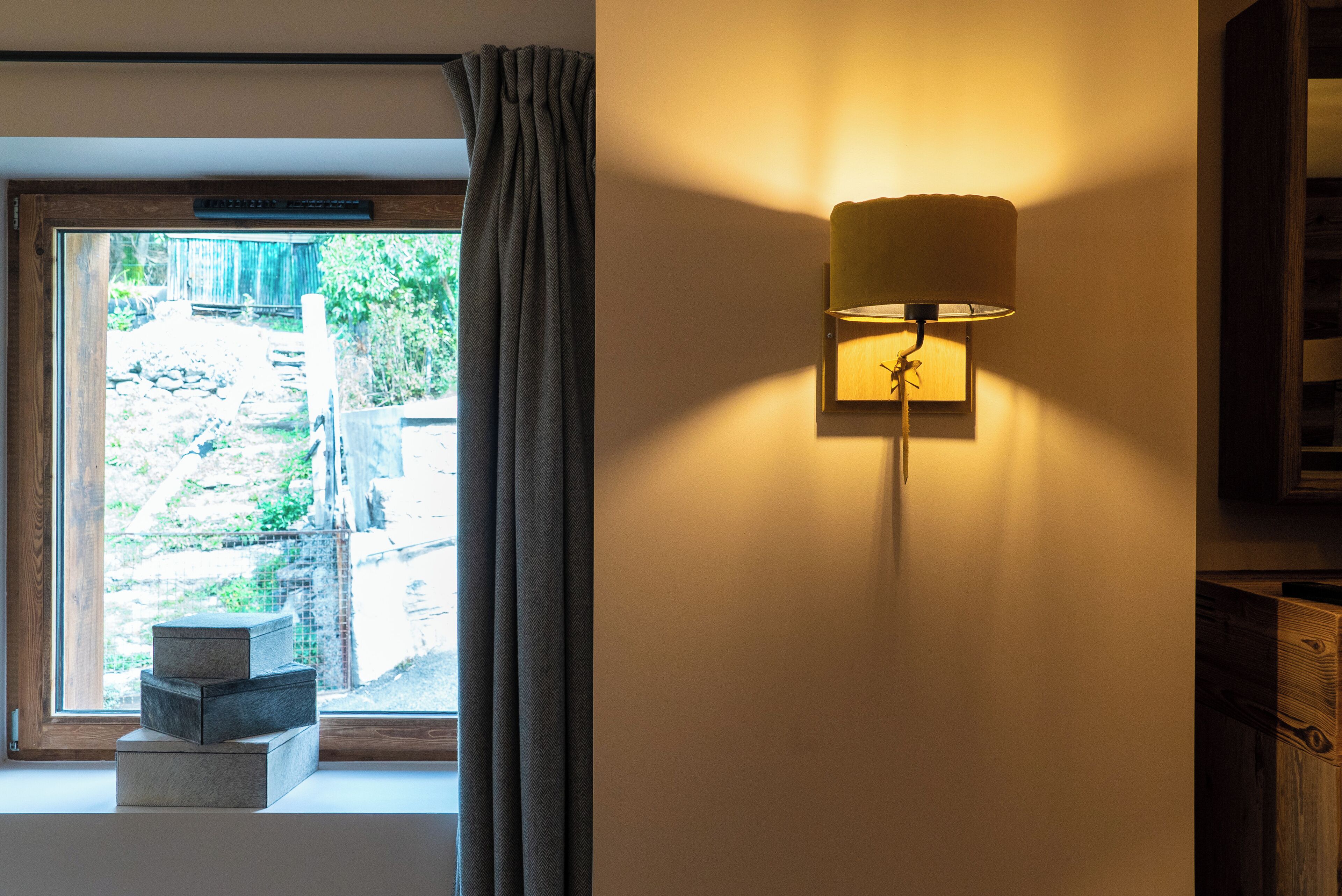 A room with a window, a wall-mounted lamp, and a small wooden structure near the window.