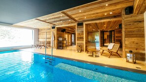 Een houten blokhut met een zwembad, een houten terras en ligstoelen.