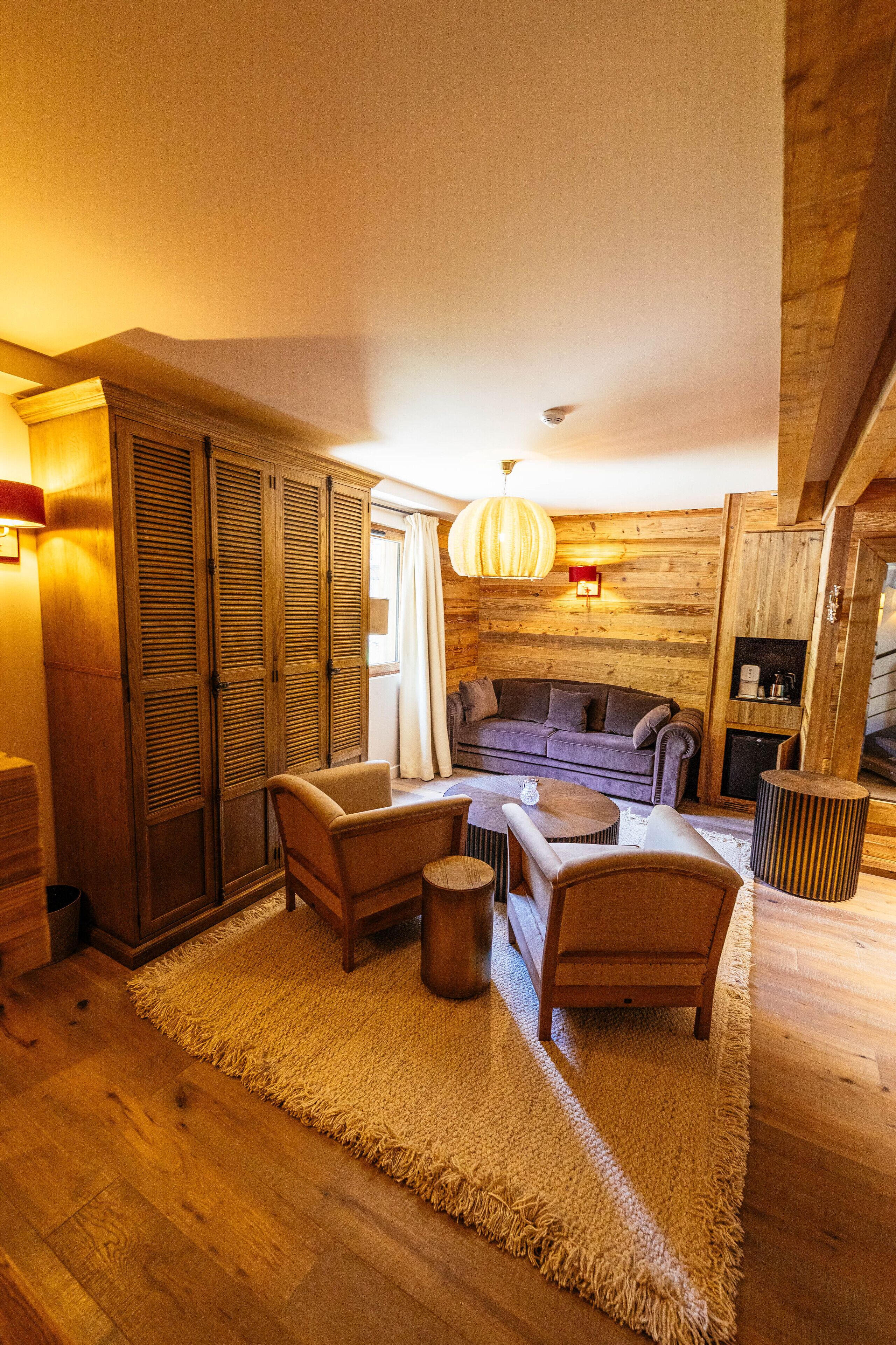 L’intérieur d’un chalet confortable, avec des murs en bois, un canapé, des fauteuils, une petite table et un luminaire suspendu.