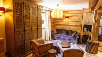 L’intérieur d’un chalet confortable, avec des murs en bois, un canapé, des fauteuils, une petite table et un luminaire suspendu.
