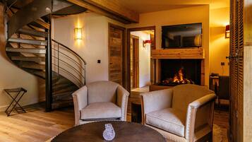 Una sala de estar moderna con una escalera espiral de madera, una chimenea y un televisor grande montado encima.