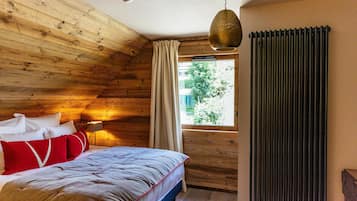 A wooden-paneled bedroom with a bed, a window with curtains, a radiator, and a hanging light fixture.