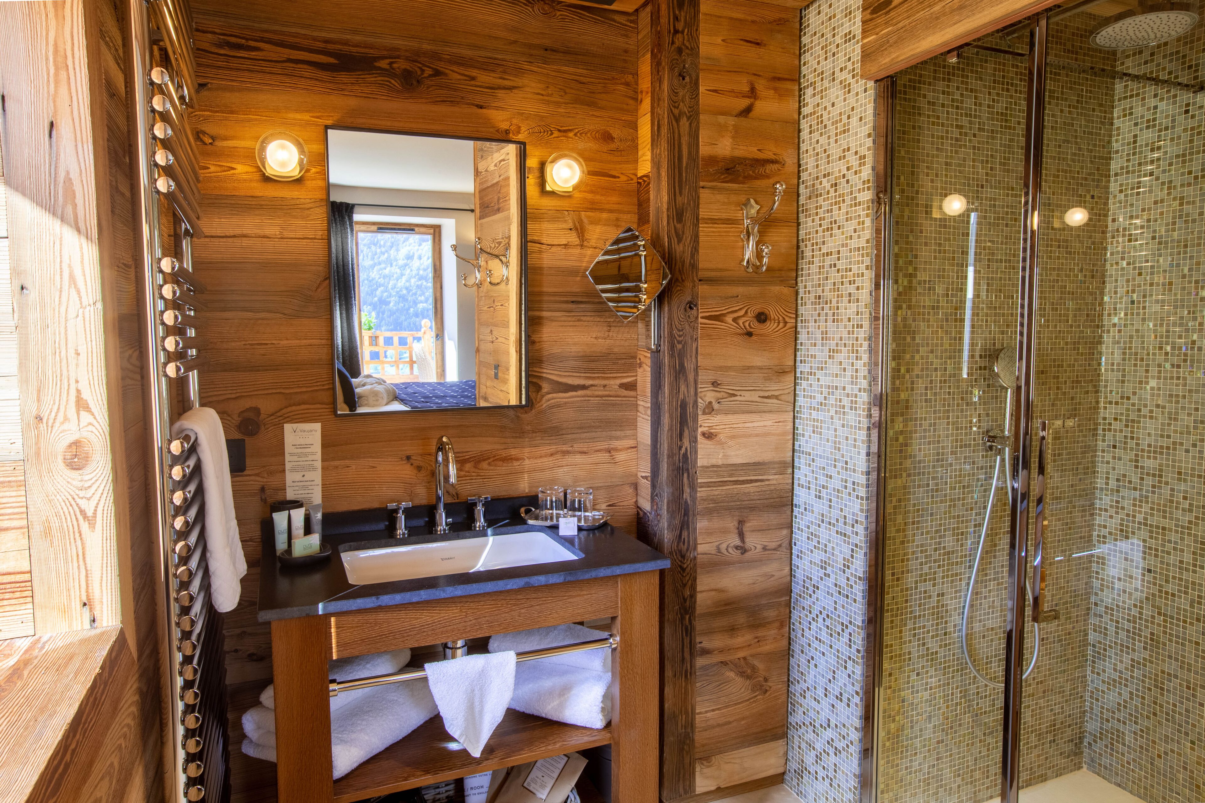 A wooden bathroom with a sink, mirror, and shower.