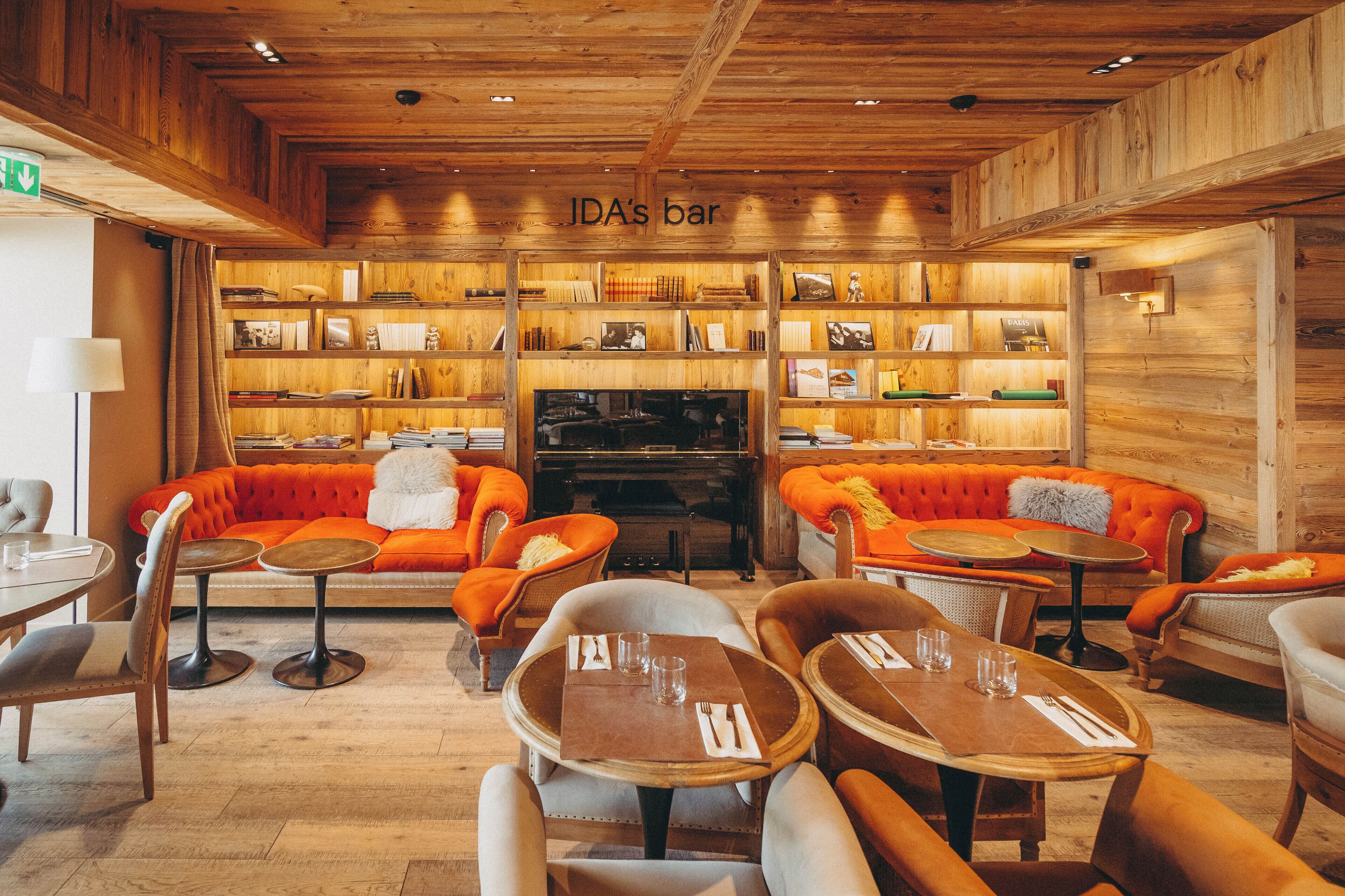 Un rincón acogedor con bar, paredes de madera, sofás naranja y mesas preparadas para comer.