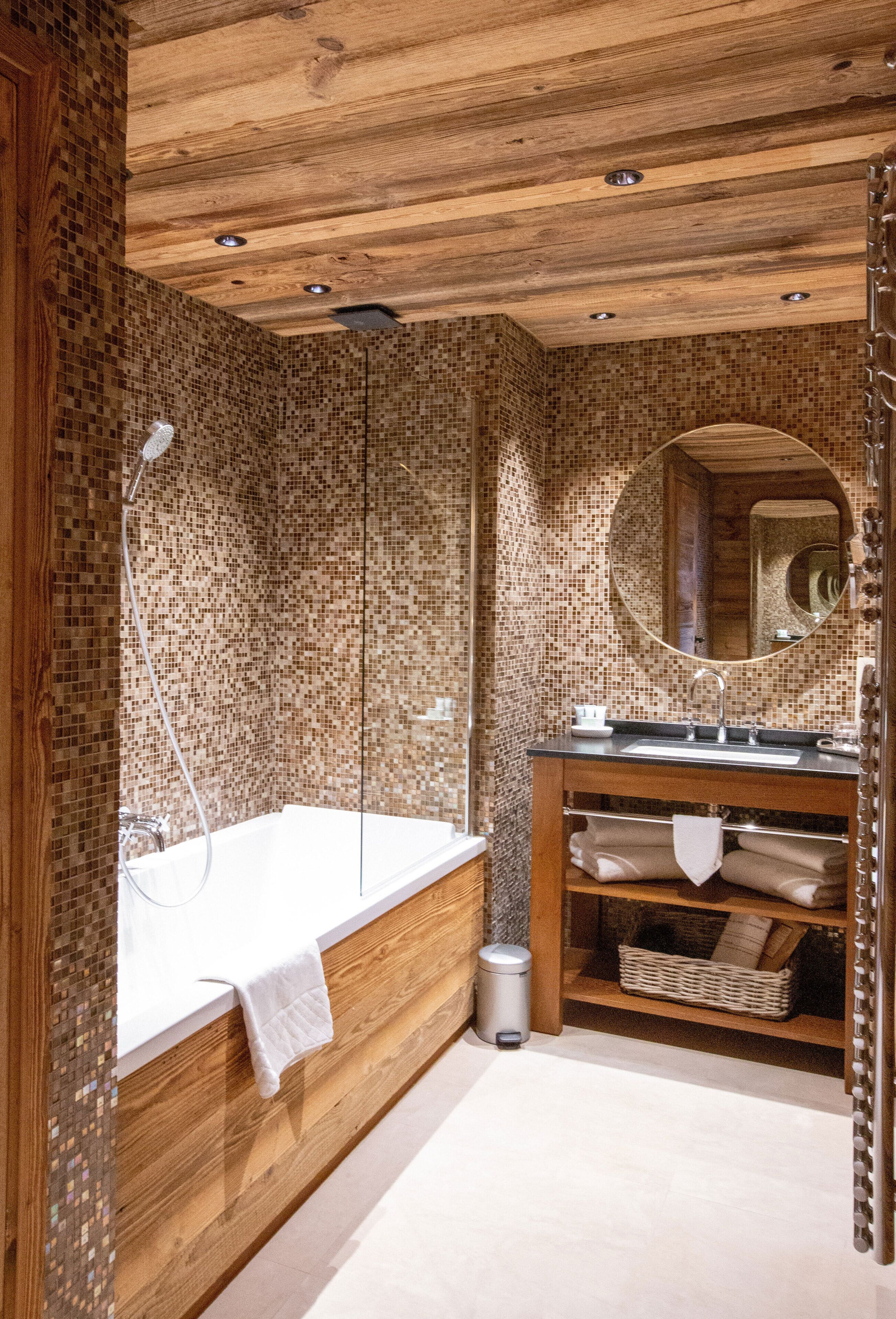 A bathroom with a wooden vanity, a large mirror, and a tiled wall.