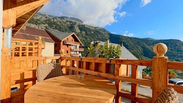 A wooden deck with a table and chairs, overlooking a mountainous landscape.