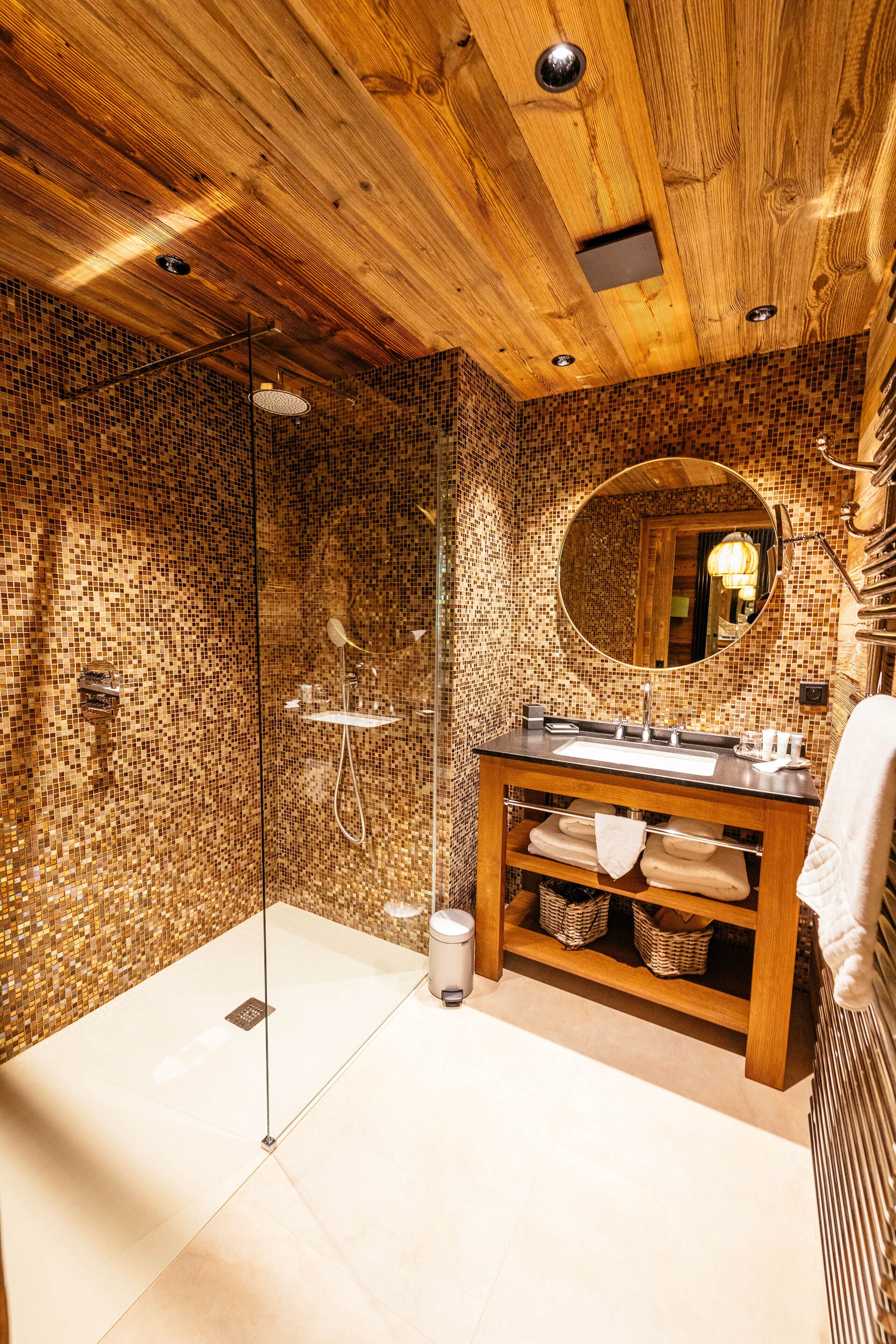 Een moderne badkamer met een houten plafond, mozaïek wandtegels, een douche met glazen wanden en een houten wastafelmeubel met spiegel.