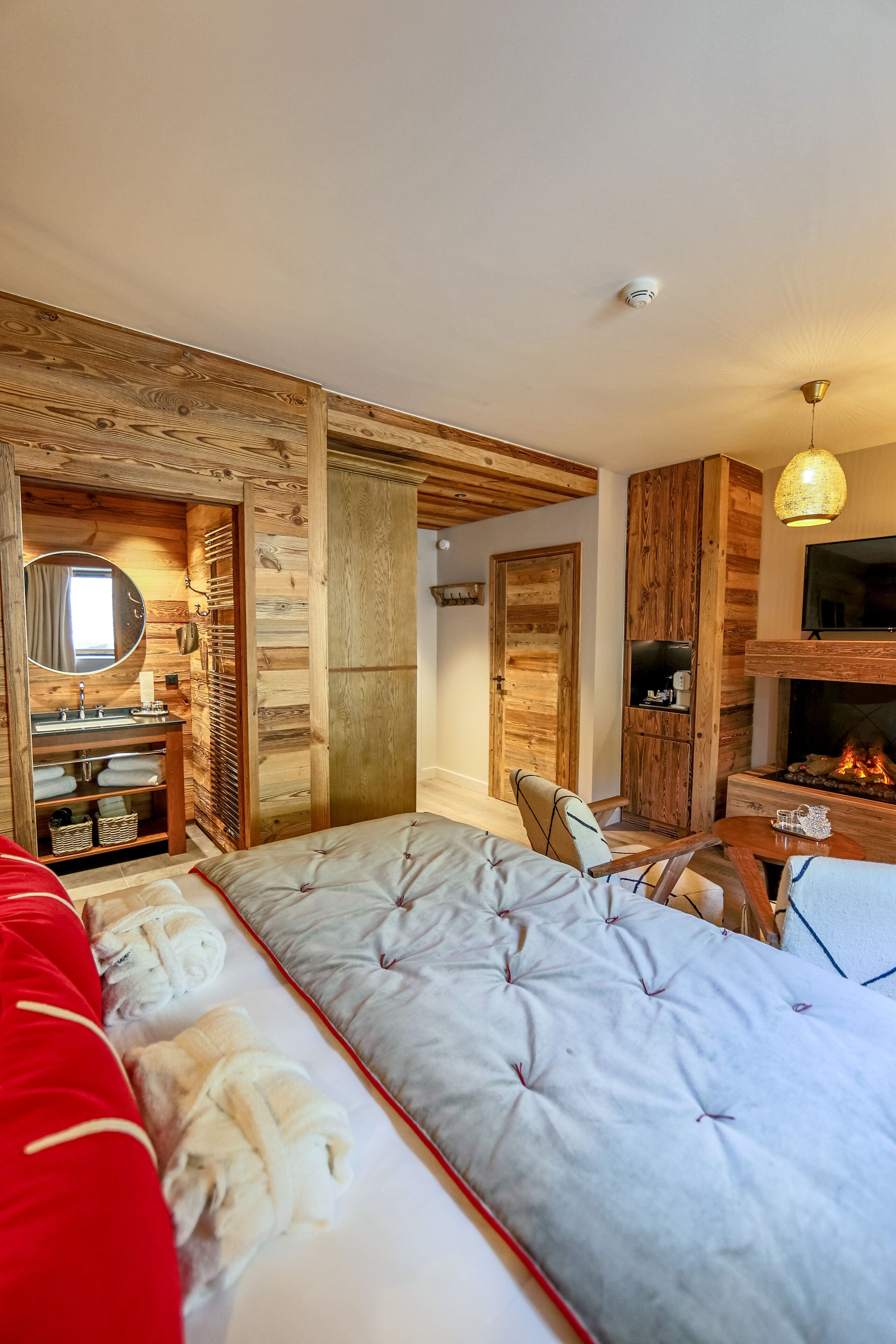 A cozy bedroom with a bed, a wooden wardrobe, a mirror, a fireplace, and a television.