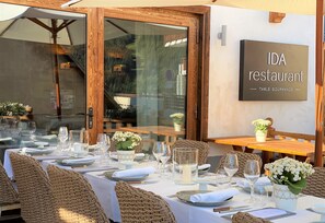 A restaurant setting with tables set for dining, a sign indicating 'IDA restaurant', and a view through a glass door. - Hotel V de Vaujany (Vaujany)