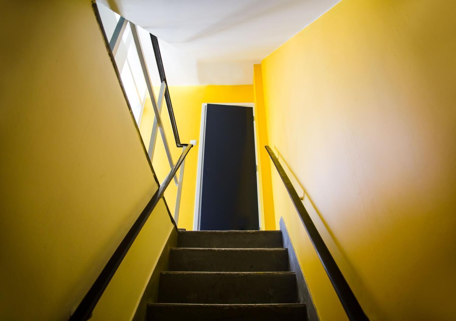 A staircase with black steps and metal handrails, leading to a dark door at the top.