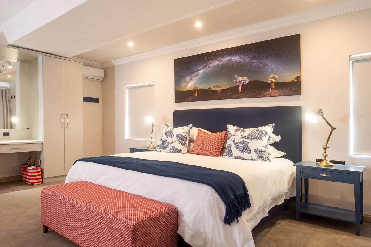 A bedroom with a large bed, a nightstand, a dresser, a mirror, and a wall with a starry night sky painting.