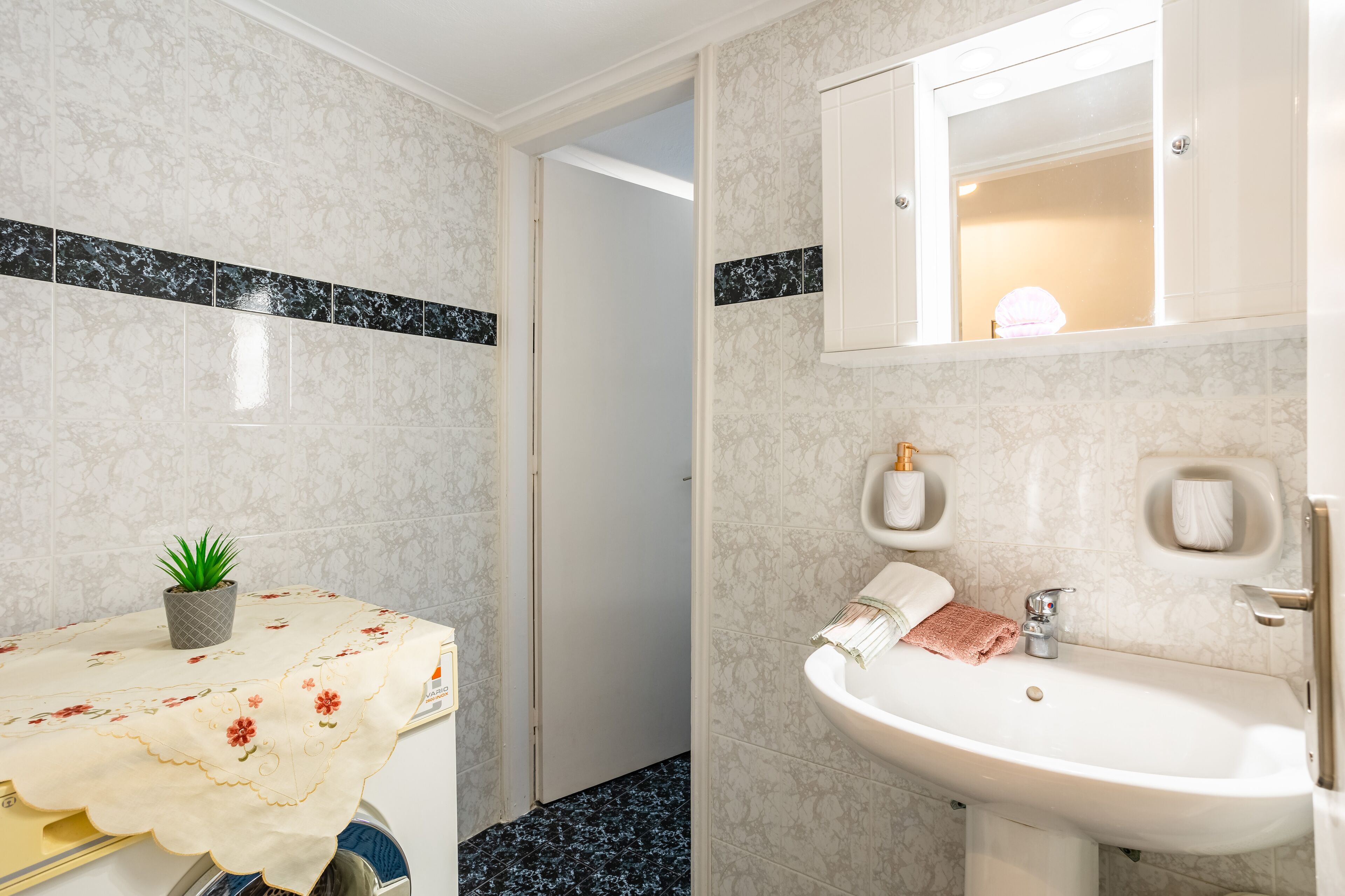 Un baño con lavabo, espejo y planta en maceta.