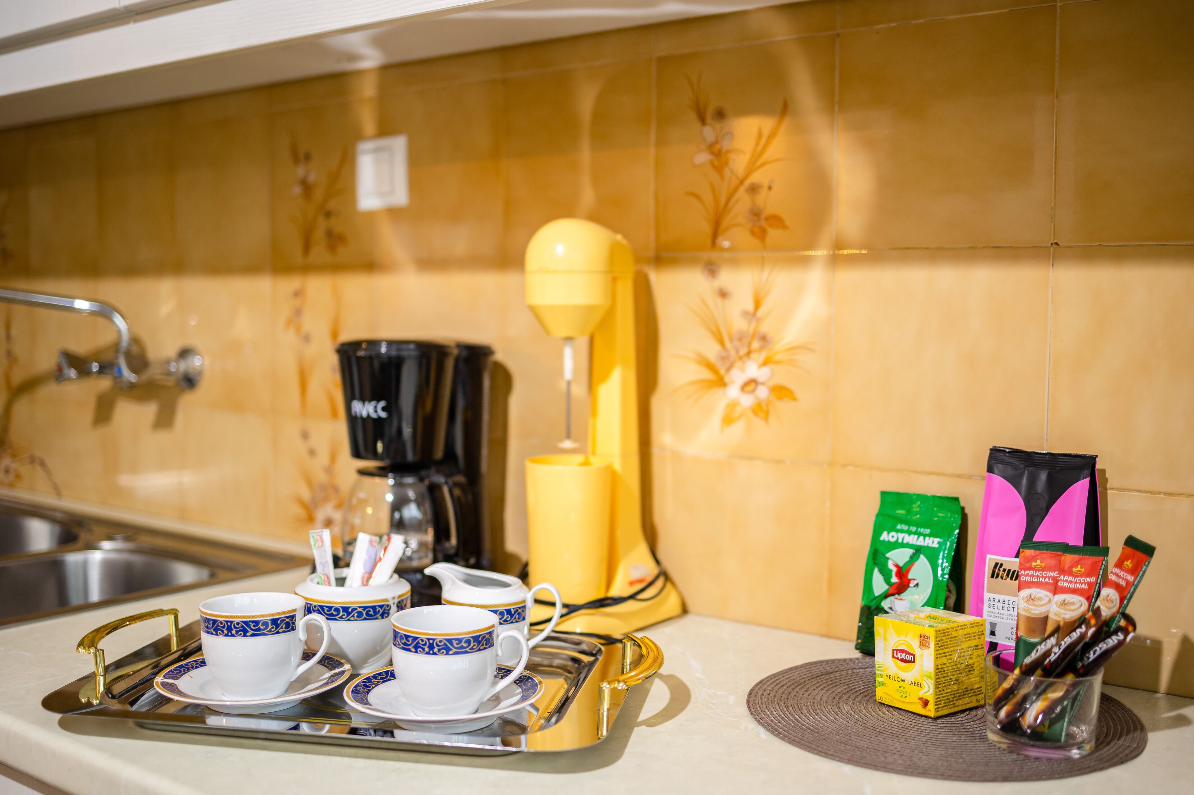 Un plan de travail de cuisine avec une machine à café, un batteur électrique jaune et divers produits à base de café et de thé.
