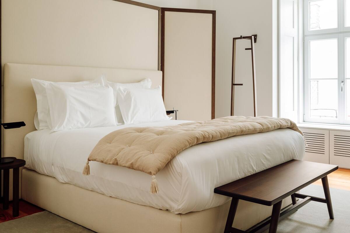 A modern bedroom with a large bed, bedside tables, a bench, and a window.