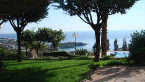 Um jardim ajardinado com piscina, árvores e vista para o mar.
