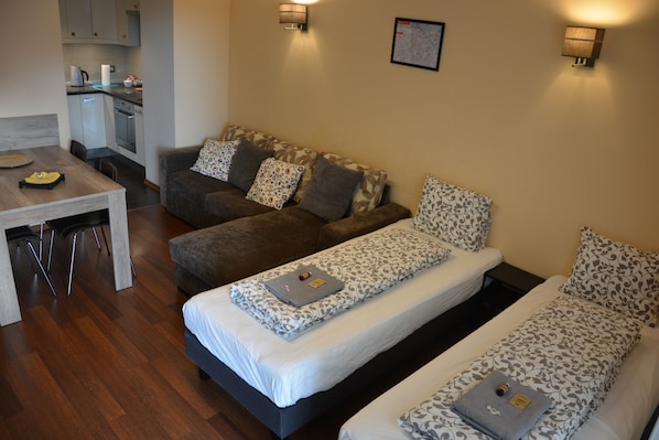 Et moderne hotelværelse med to enkeltsenge, en sofa, et spiseområde og et tekøkken.