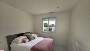 A bedroom with a bed, pillows, a window, and a small rug. - Mediterranean-style villa with pool (Agde)