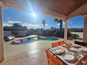 A covered outdoor patio with a pool, dining table set for four, and a view of the neighborhood. - Mediterranean-style villa with pool (Agde)