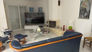 A living room with a blue sofa, a glass coffee table, a flat-screen TV, a fireplace, and a painting on the wall. - Mediterranean-style villa with pool (Agde)