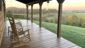 Een houten terras met schommelstoelen met uitzicht op een landelijk gebied tijdens zonsondergang.