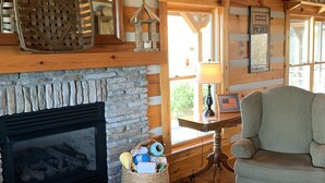Een gezellig interieur van een chalet met een stenen openhaard, houten wanden, een geweven mand met wol en een gestreept fauteuil.