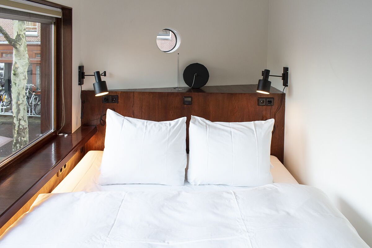 Una habitación de hotel con una cama, dos lámparas de noche, un espejo redondo y vistas a bicicletas afuera.