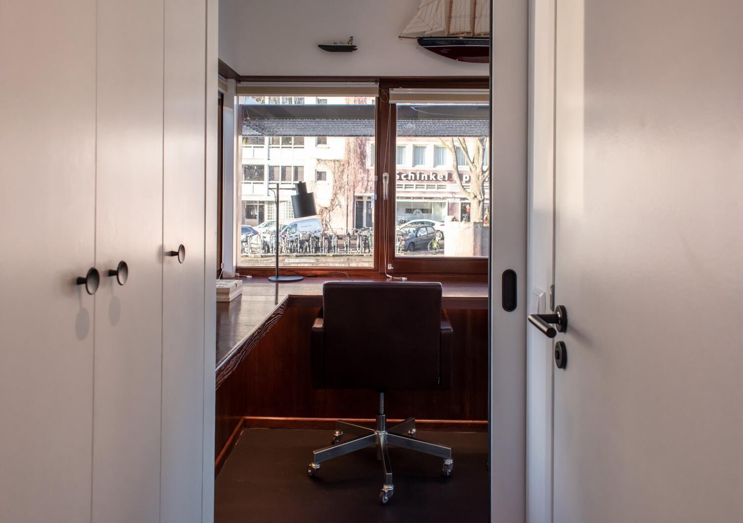 Un espacio de oficina moderno con un escritorio y una silla, ventanas amplias con vistas a bicicletas y edificios.