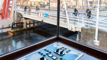 A control panel with multiple buttons and switches, a window overlooking a canal with a bridge and buildings in the background.
