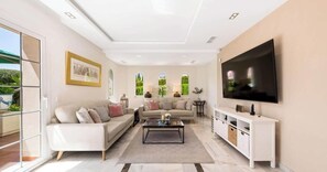 A modern living room with a large flat-screen TV, a sofa set, a coffee table, and a white entertainment unit.