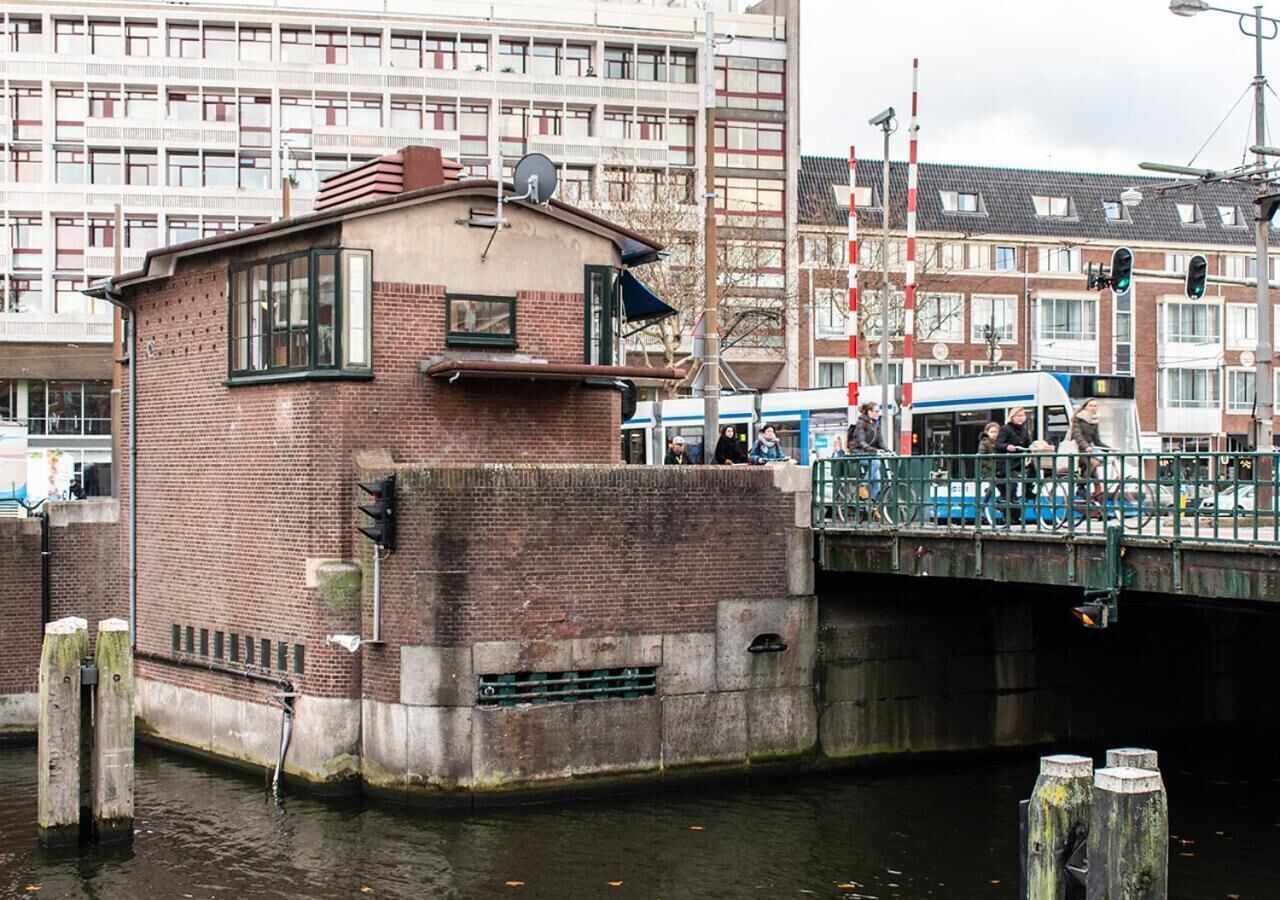 Un bâtiment en briques avec une petite fenêtre et une porte, situé près d’un canal et d’un pont.