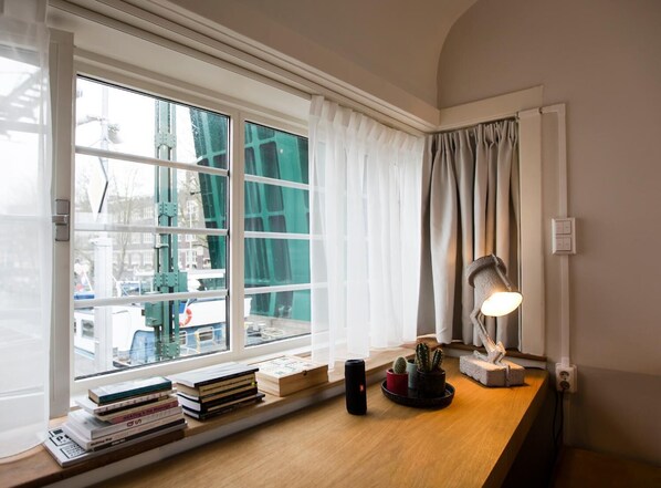 A room with a large window, a desk with books, a lamp, and a cactus plant. - SWEETS - Kinkerbrug (Amsterdam)