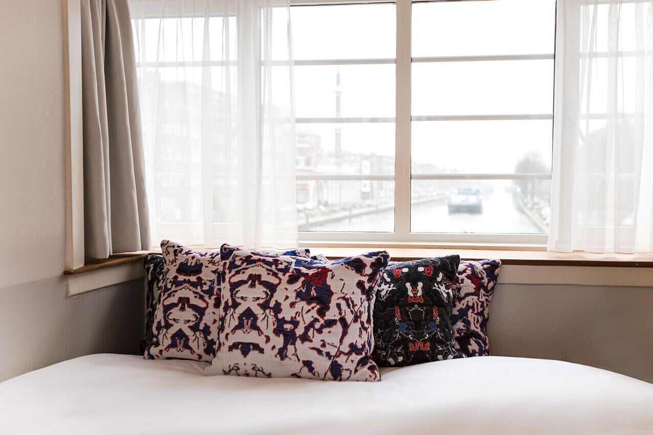 A bed with patterned pillows and a view of a cityscape through a window.