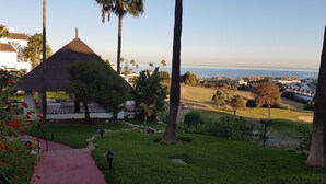 A view of a golf course with a thatched-roof pavilion, palm trees, and a distant ocean view.